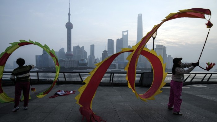 People fly dragon-shaped kites on the Bund in front of buildings in Pudong’s financial district in Shanghai, China